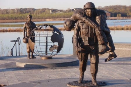 Bronze military memorial soldier carrying wounded soldier statue with female military nurse statue and world globe monument