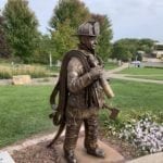 Bronze firefighter in uniform with gear and fire hose statue