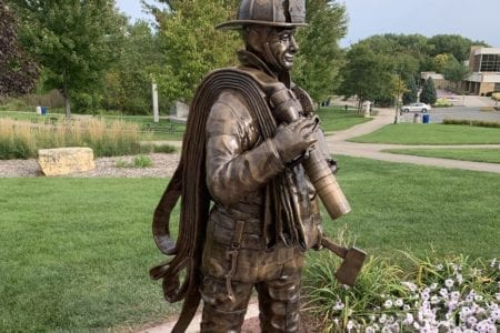 Bronze firefighter in uniform with gear and fire hose statue