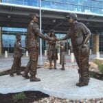 Bronze military memorial soldier statue shaking the hand of veteran statue with mom and child looking on