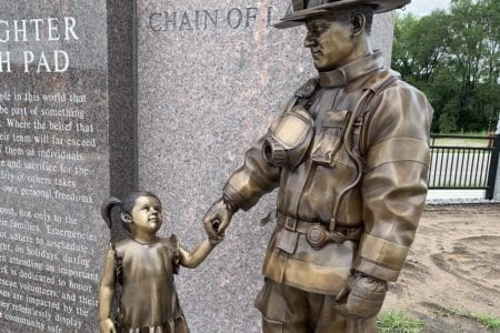 Bronze firefighter monument in uniform with equipment holding child statue