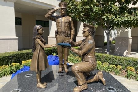 Bronze kneeling police officer presenting flag to child and saluting police officer in uniform statues