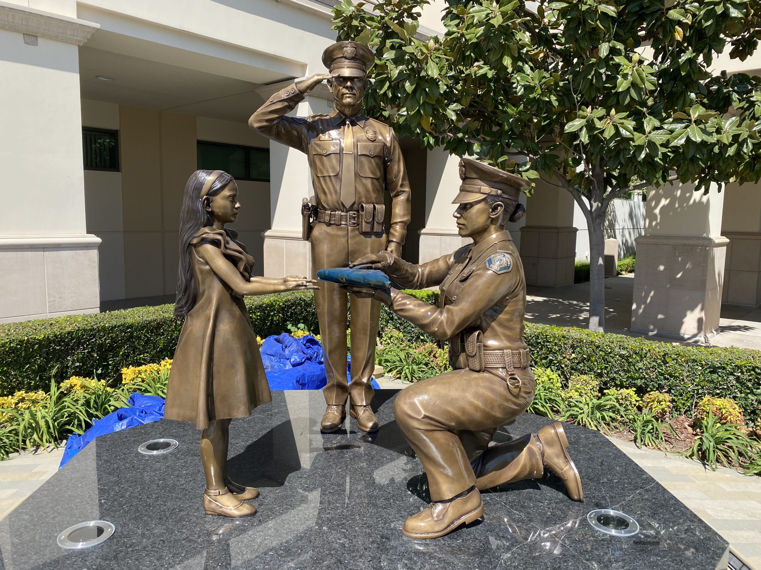 Bronze kneeling police officer presenting flag to child and saluting police officer in uniform statues