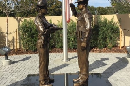 Bronze law enforcement honor guard statues: deputy presenting the flag and deputy saluting.