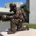 Bronze kneeling firefighter in full uniform holding helmet statue