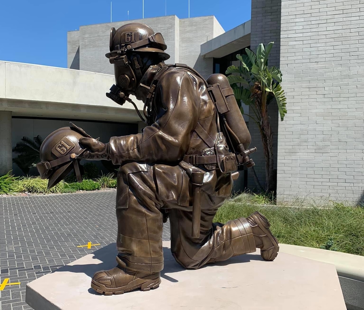 Bronze kneeling firefighter in full uniform holding helmet statue