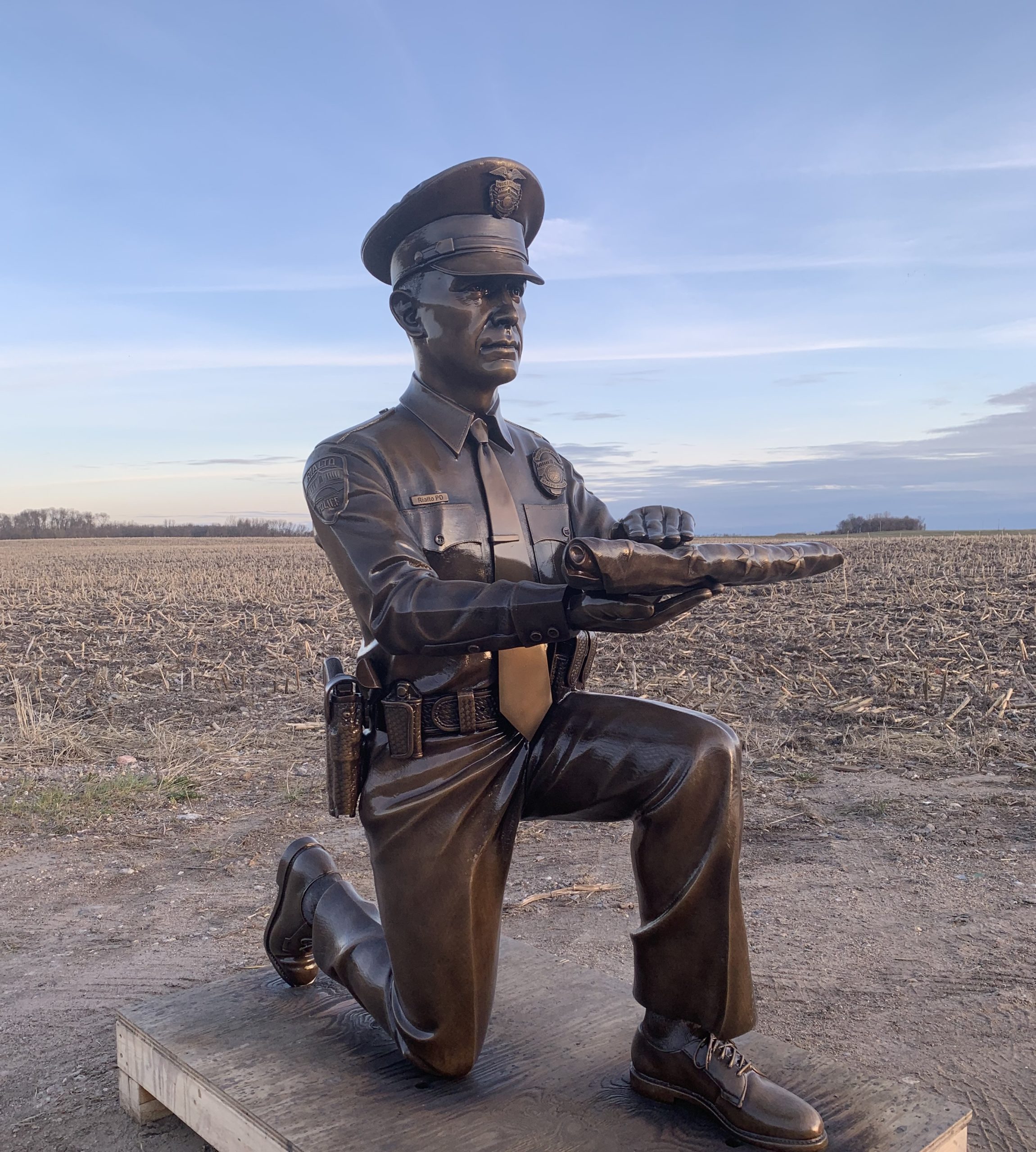 Bronze kneeling police officer statue in uniform presenting flag