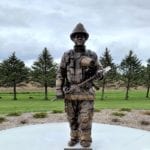 Bronze firefighter memorial statues in uniform with gear holding axe statue
